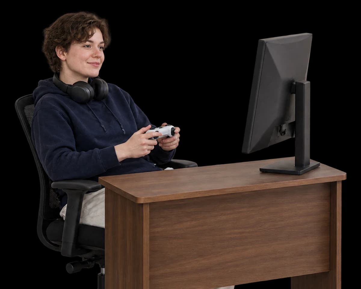 A game developer leans back at their desk holding a controller.